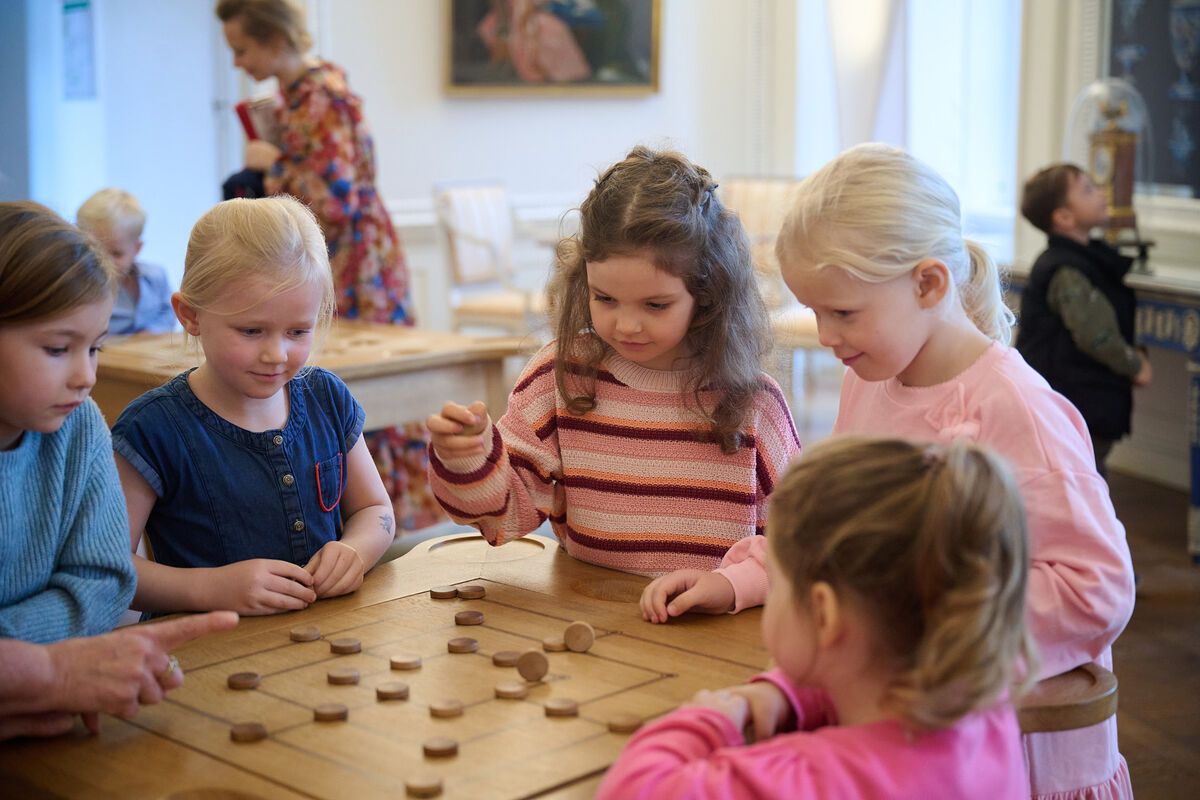 Eine Gruppe mit Kindern sitzt an einem rekonstruierten Spieltisch. Sie probieren alte Brettspiele aus.