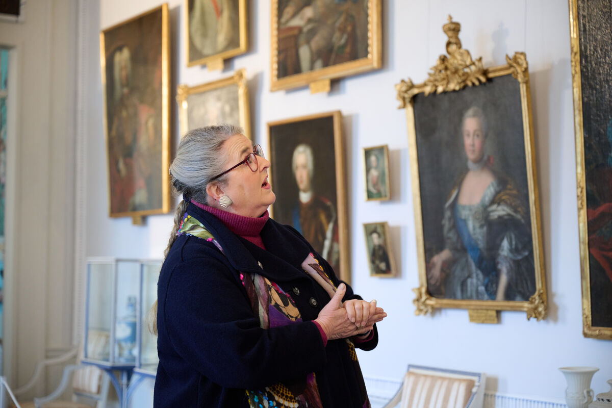 Eine Schlossführerin steht vor einer Wand mit Gemälden und Porträts und erzählt die Geschichten dazu.